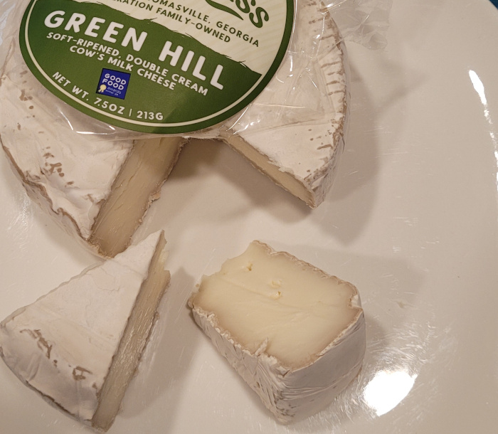 A wheel of the cheese cut into wedges. White rind and off-white paste. The dairy label is also visible.