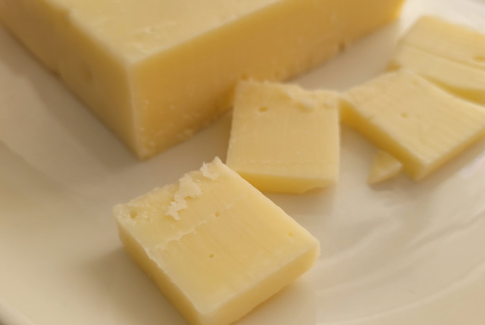 Photo of cheese cut into pieces on a white plate. Soothing light yellow color.