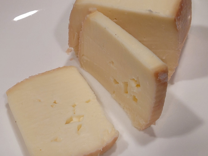 A block of the cheese cut into several slices showing some holes and a dull orange rind.