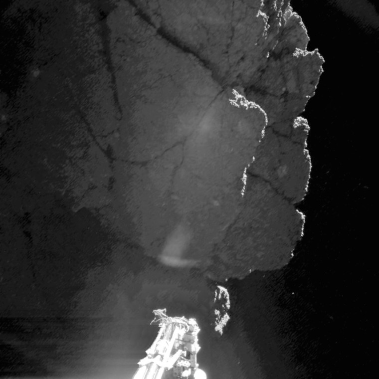 the outline of deeply fractured rock and ice, the darkness of space in the background, and a lander foot brightly lit by the sun.