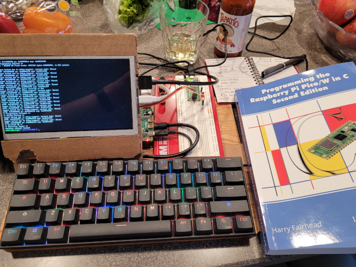 photo at the kitchen counter with the aforementioned book and my cool cardboard computer setup with pi pico and LEDs